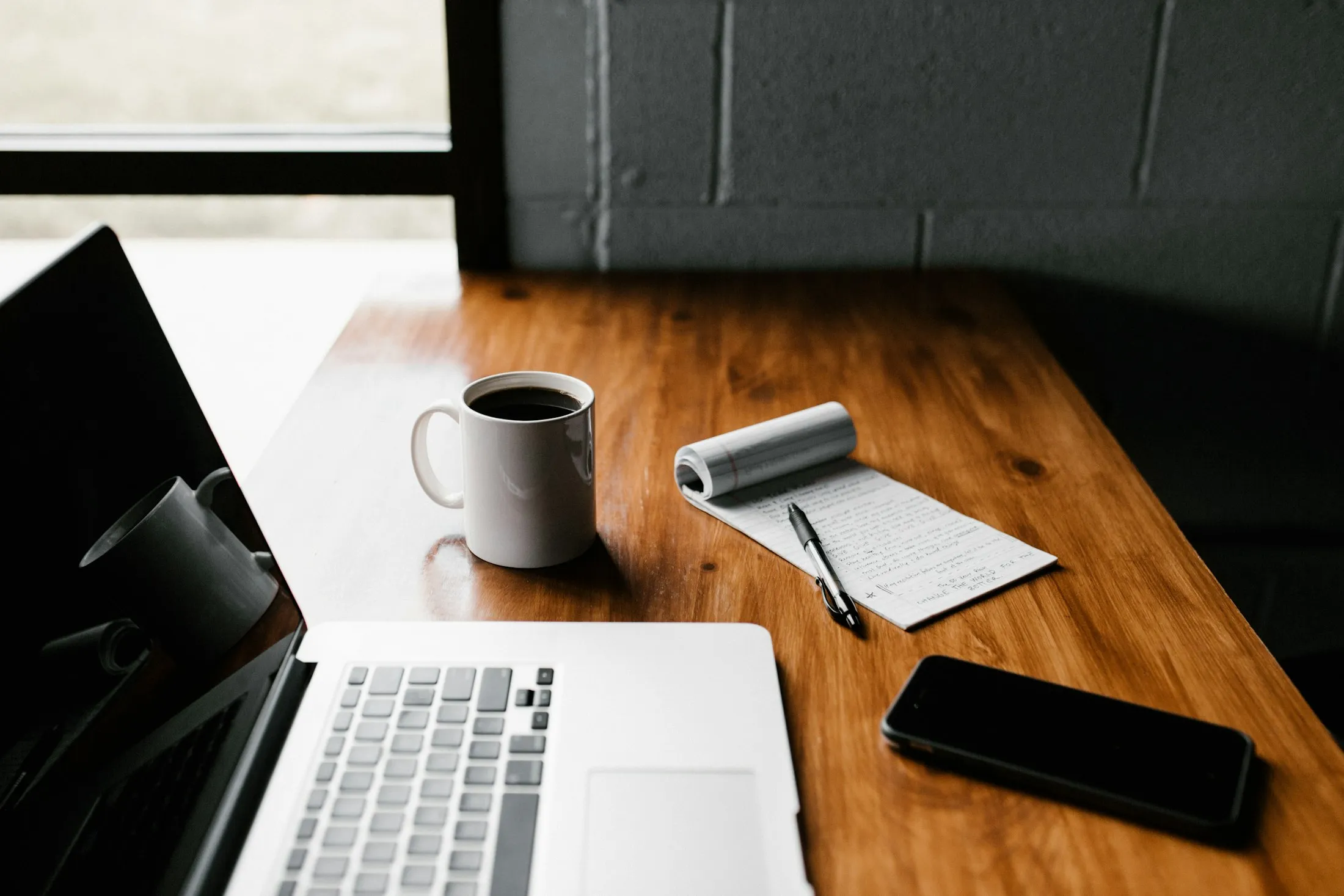 A laptop, coffee and phone on a wooden desk