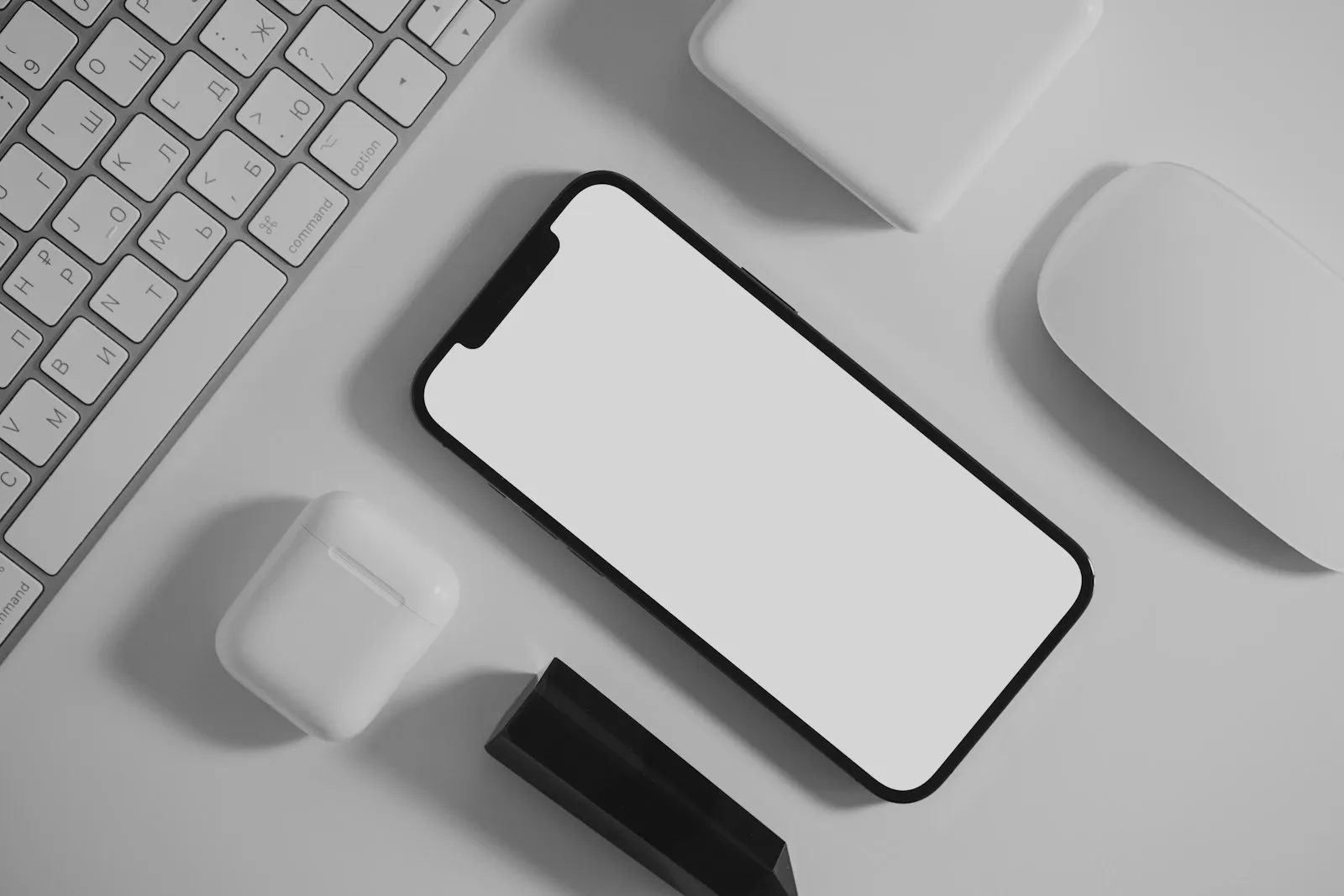 A smartphone next to a keyboard and earbuds on a white desk